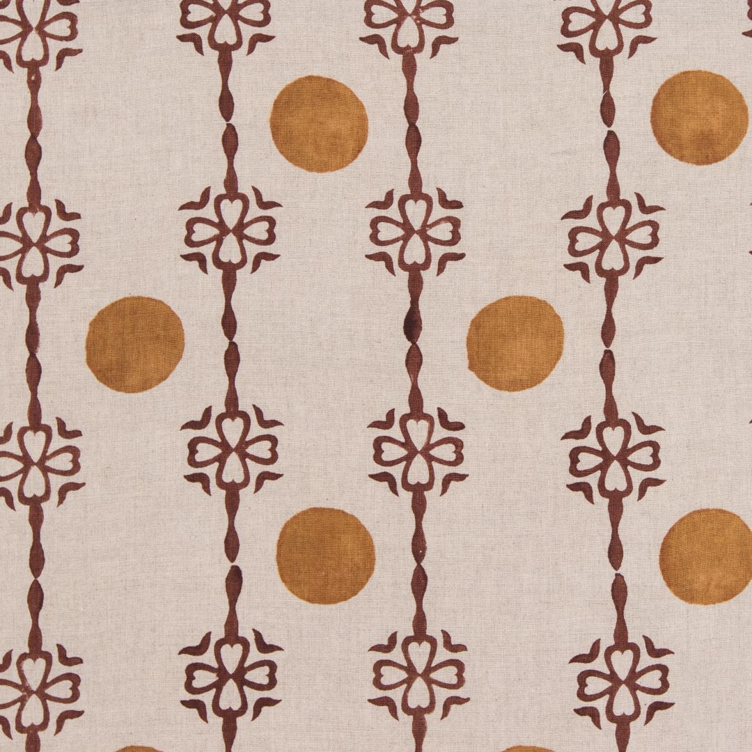 Detail of fabric in a linear flower and circle print in burnt orange and rust on a cream field.