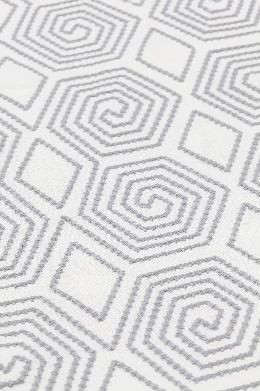 Detail of an embroidered fabric with a geometric spiral design in grey on a white field.