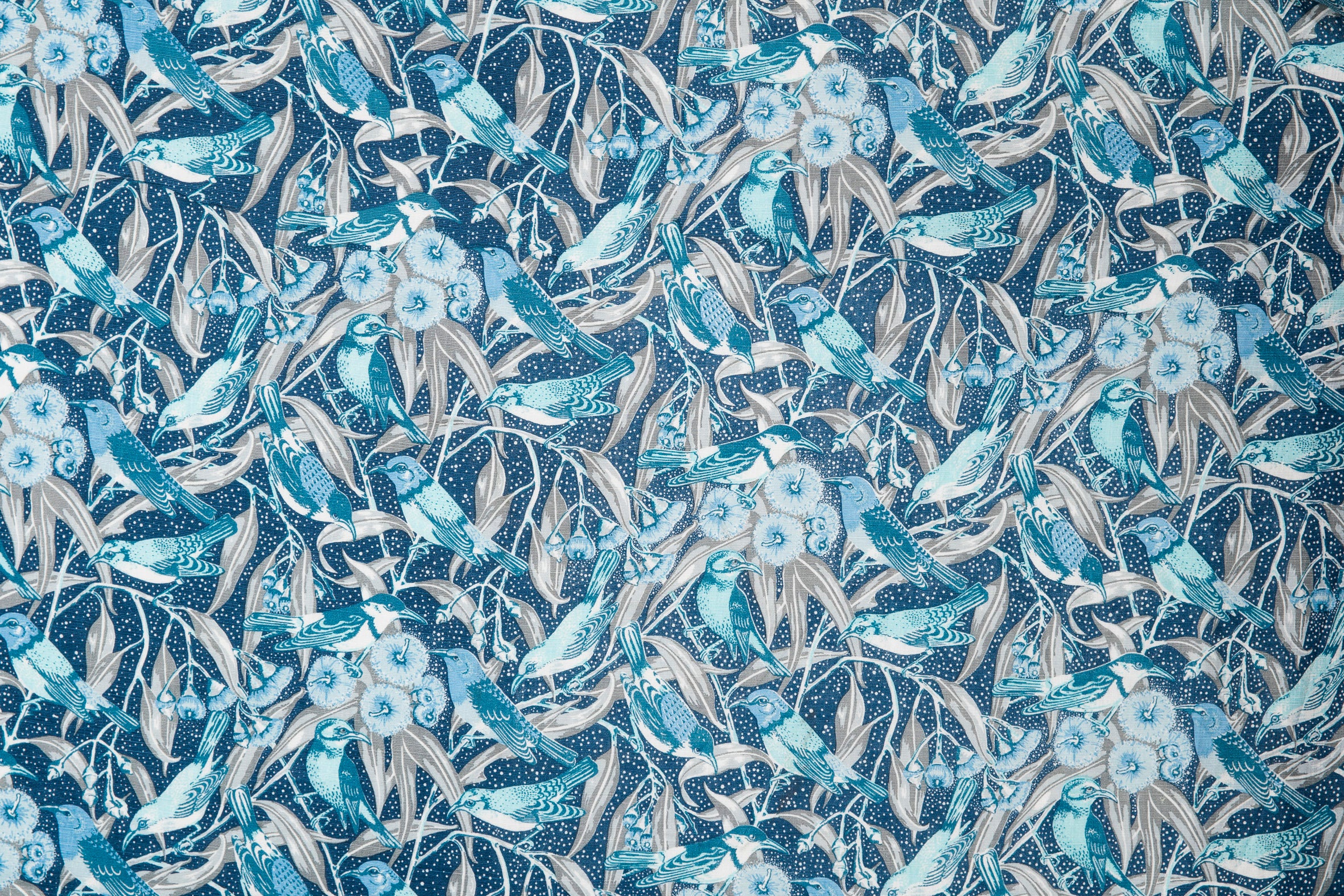 Fabric detail of a dense bird and branch pattern in shades of blue, turquoise and grey.