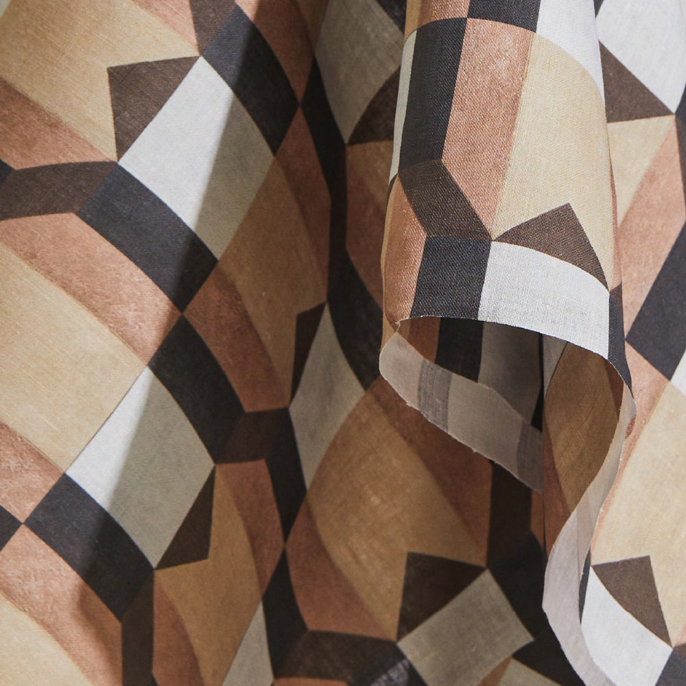 Draped fabric yardage in a large-scale geometric grid in shades of cream, brown and peach on a white field.
