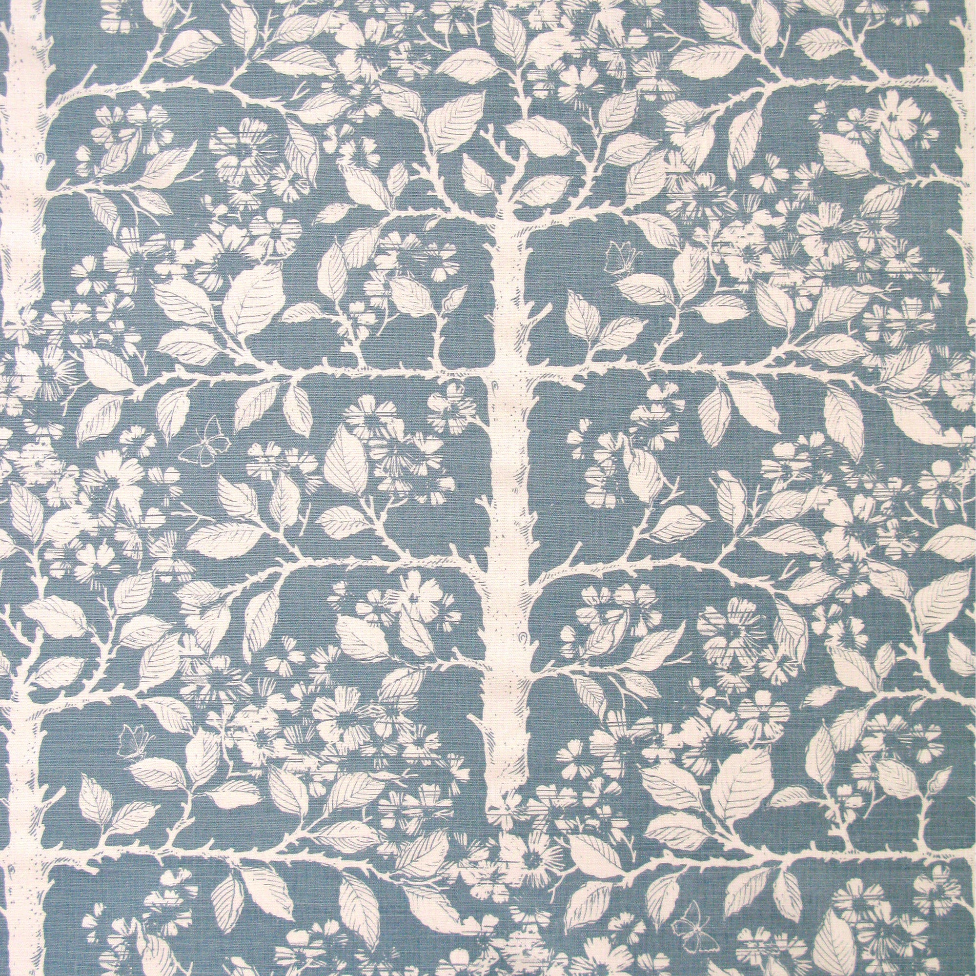 Detail of fabric in a large-scale tree and leaf print in cream on a blue field.
