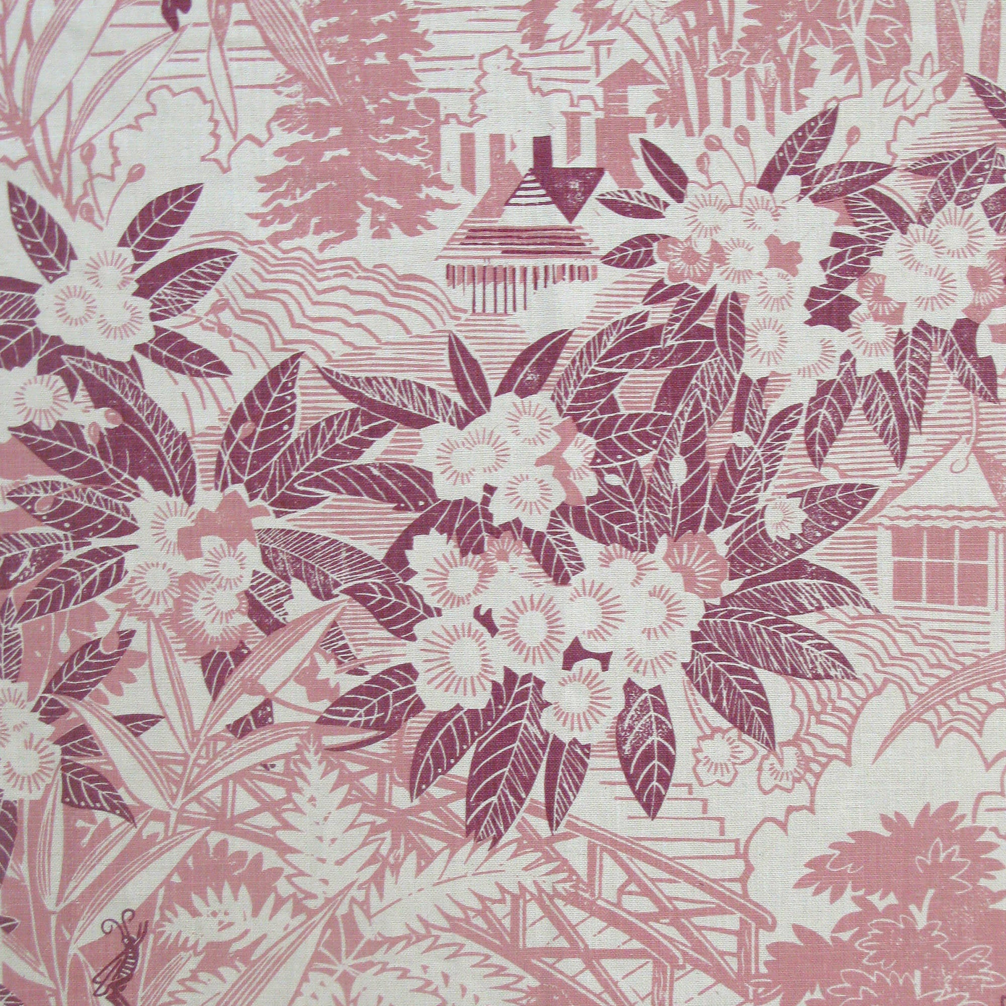 Detail of fabric in an intricate botanical, bridge and house print in pink and maroon on a cream field.