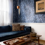 A maximalist living room tableau with walls papered in an abstract textural print in blue, navy and black.