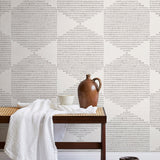 A bench with a towel and clay vases stands in front of a wall papered in a geometric star print in light gray and cream.