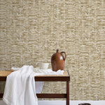 A bench with a towel and clay vases stands in front of a wall papered in a textural checked print in brown and white.