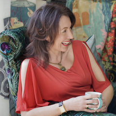Side profile of a brunette woman wearing a red top, seated in a patterned chair and laughing.
