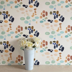 Wall paper with a thumbprint pattern in colors of brown, yellow, green and blue, with a white vase of flowers sitting in front.