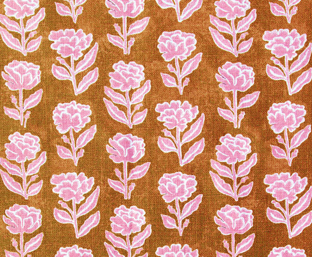 Detail of fabric in a classic floral print in bright pink and white on a rust orange field.