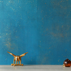 A winged bronze horse statue sits in front of a wall papered in bright turquoise with a gold paint splatter pattern.
