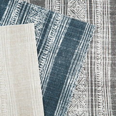 Three overlapping pieces of upholstery fabric with striped tropical patterns in cream, navy and gray on white backgrounds.