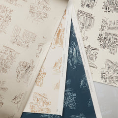 Overlapping sheets of wallpaper in shades of cream and navy with black and white illustrations, laid out on a white surface.