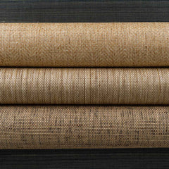 Three rolled pieces of woven fabric in natural jute shades laying on a black surface.