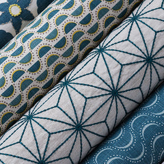 Four rows of fabrics set at a diagonal, each with a different print in variations of white, yellow and teal.