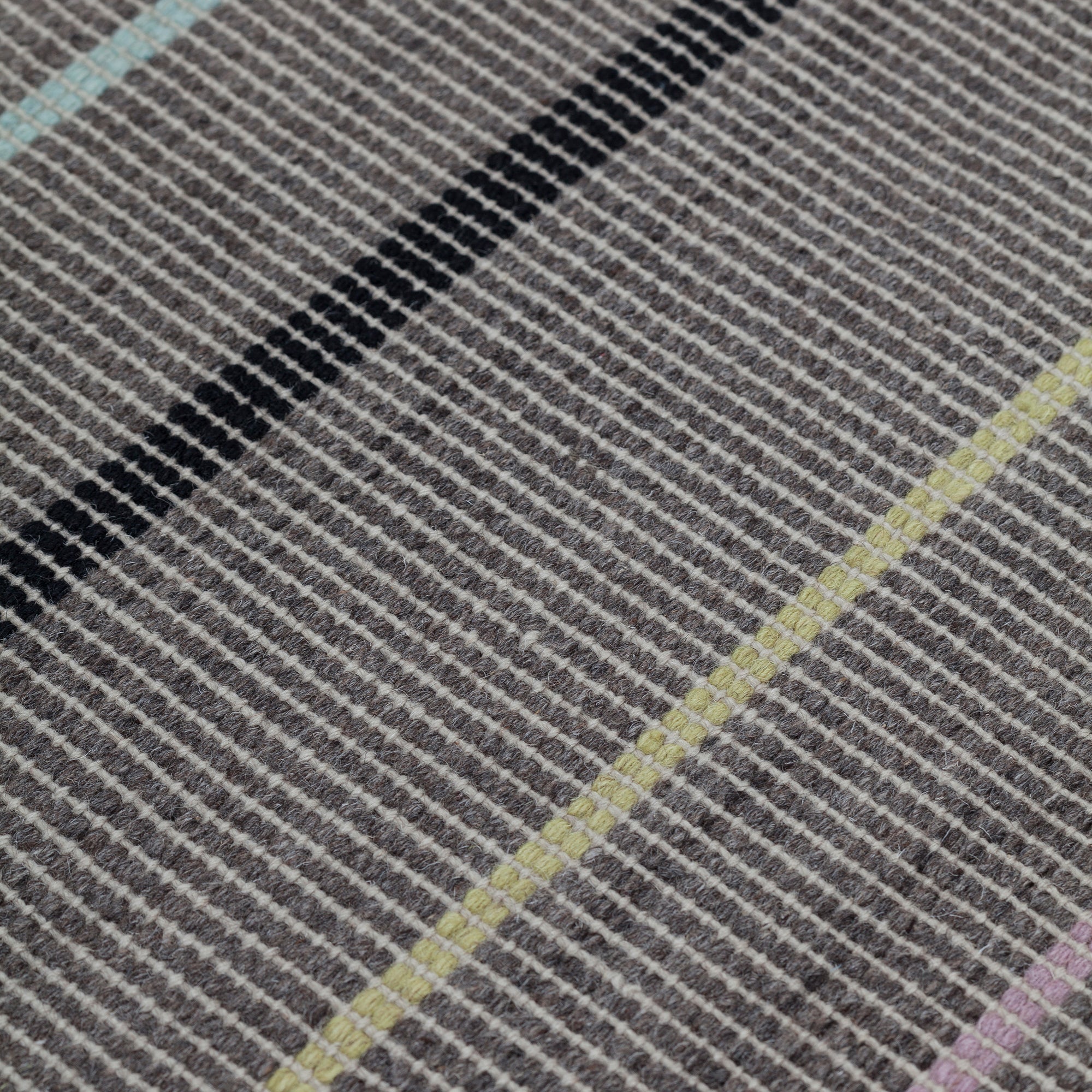 Detail of the Jasper Waffle Rug in Jet, widely spaced thin stripes of yellow, pink, black, acqua and white on a grey field.