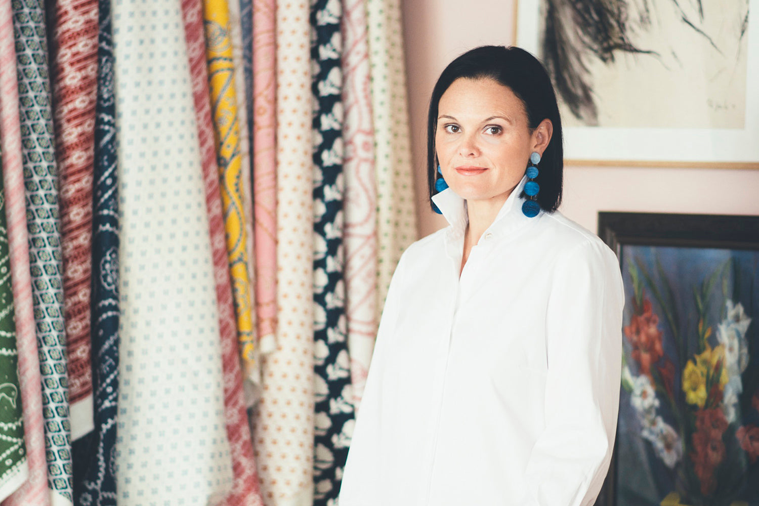 Brunette woman in an oversize white button down standing in front of a table covered in fabric swatches.