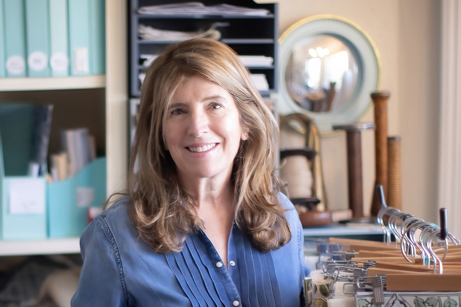 A woman with wavy brown hair and wearing a blue pleated button-down stands next to a rack with swatches of interior fabrics.