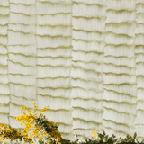 Yellow blossoms stand in front of a wall papered in an abstract textural pattern in metallic green and greige.