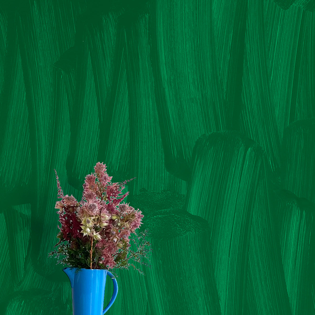 A vase of flowers stands in front of a wall papered in an abstract paint print in shades of green.