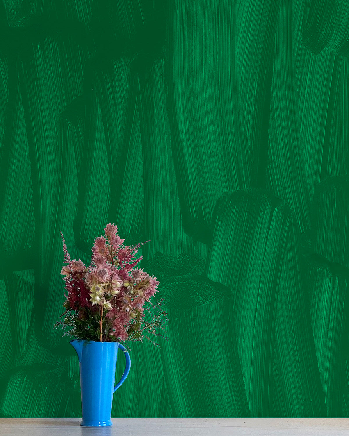 A vase of flowers stands in front of a wall papered in an abstract paint print in shades of green.