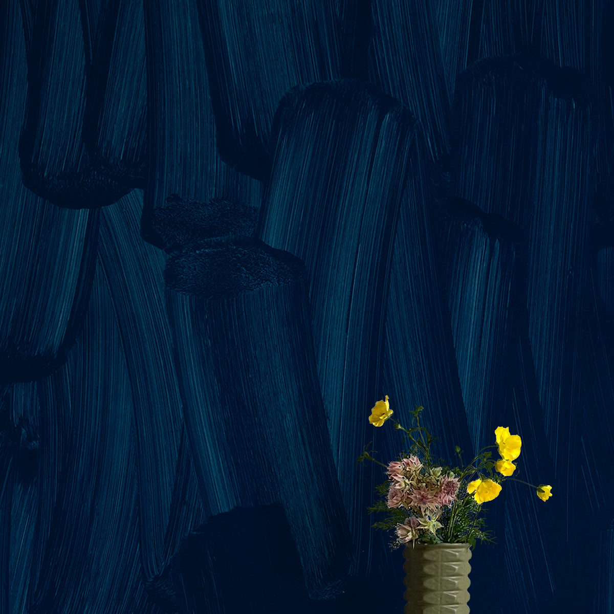 A vase of flowers stands in front of a wall papered in an abstract paint print in shades of navy.