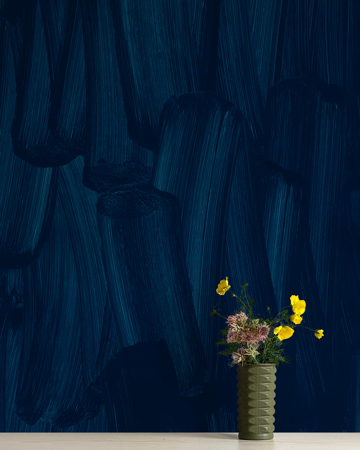 A vase of flowers stands in front of a wall papered in an abstract paint print in shades of navy.