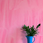 A vase of flowers stands in front of a wall papered in an abstract paint print in shades of pink.