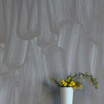 A vase of flowers stands in front of a wall papered in an abstract paint print in shades of gray.