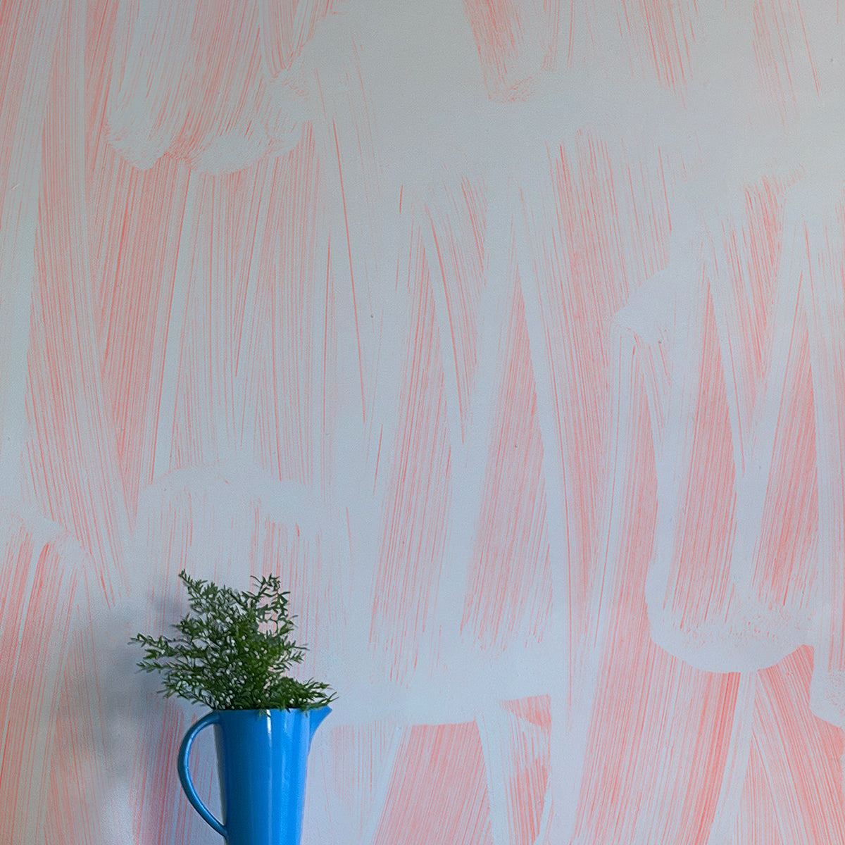 A vase of flowers stands in front of a wall papered in an abstract paint print in light blue on a pink field.