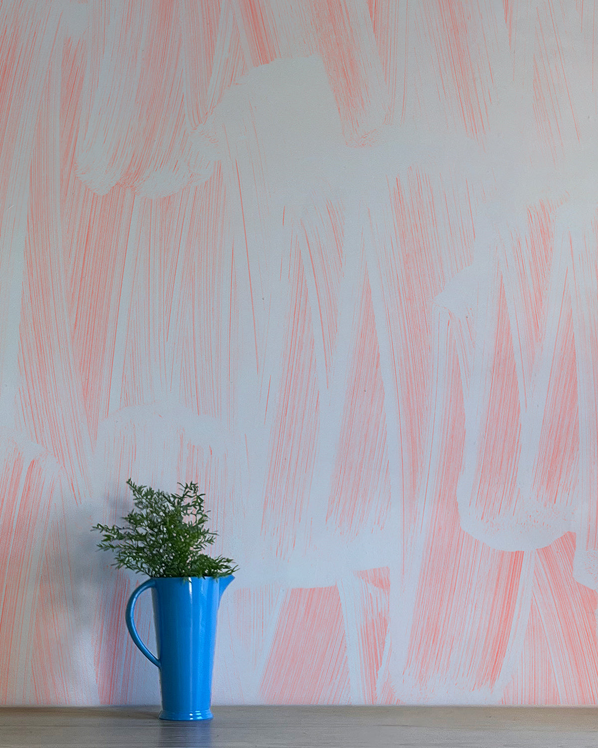 A vase of flowers stands in front of a wall papered in an abstract paint print in light blue on a pink field.