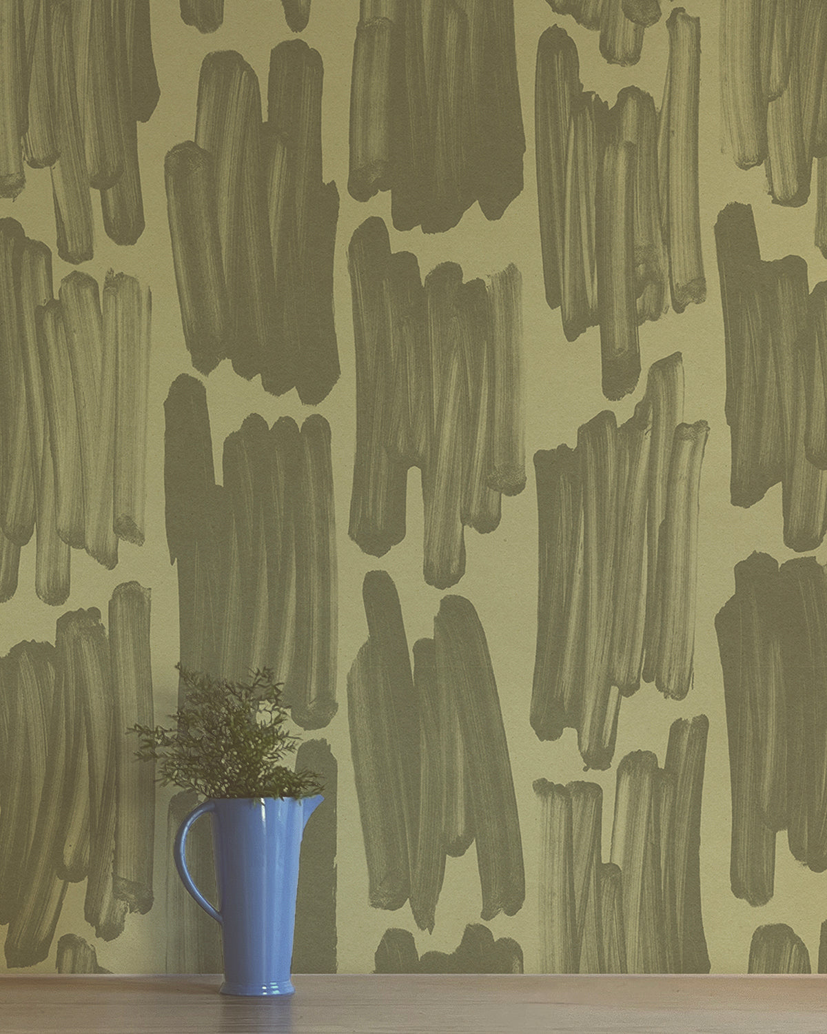 A vase of flowers stands in front of a wall papered in an abstract paint swatch print in dark green on an olive field.