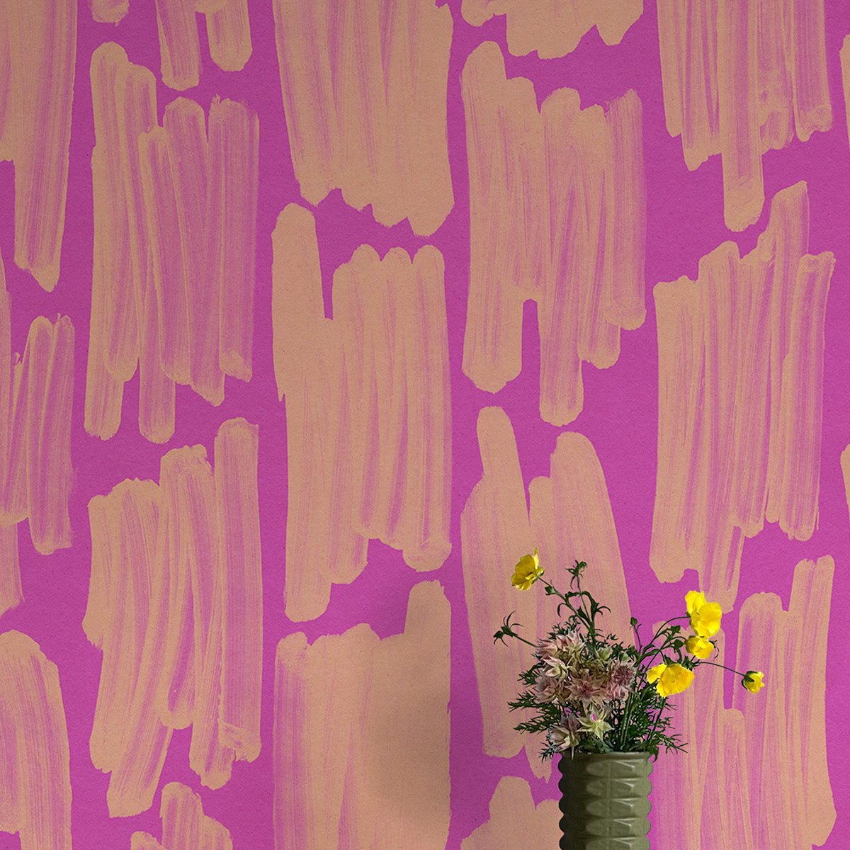 A vase of flowers stands in front of a wall papered in an abstract paint swatch print in orange on a pink field.