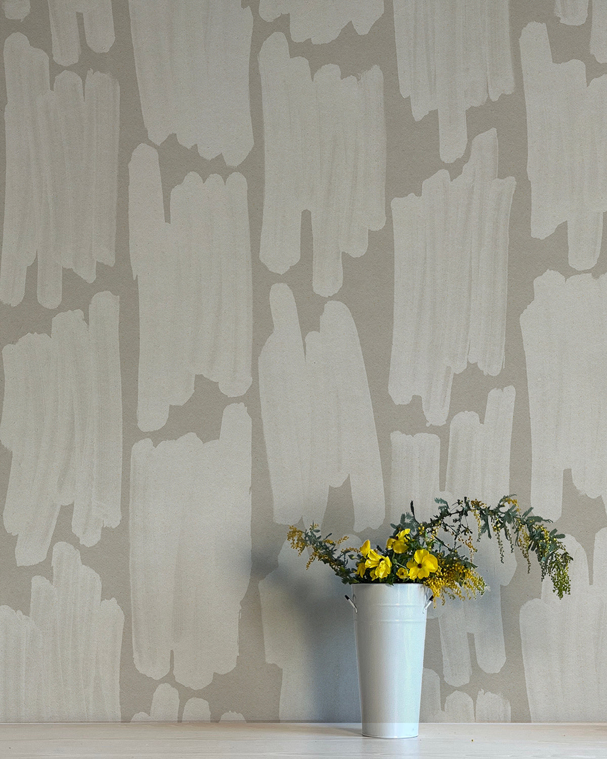 A vase of flowers stands in front of a wall papered in an abstract paint swatch print in light gray on a gray field.