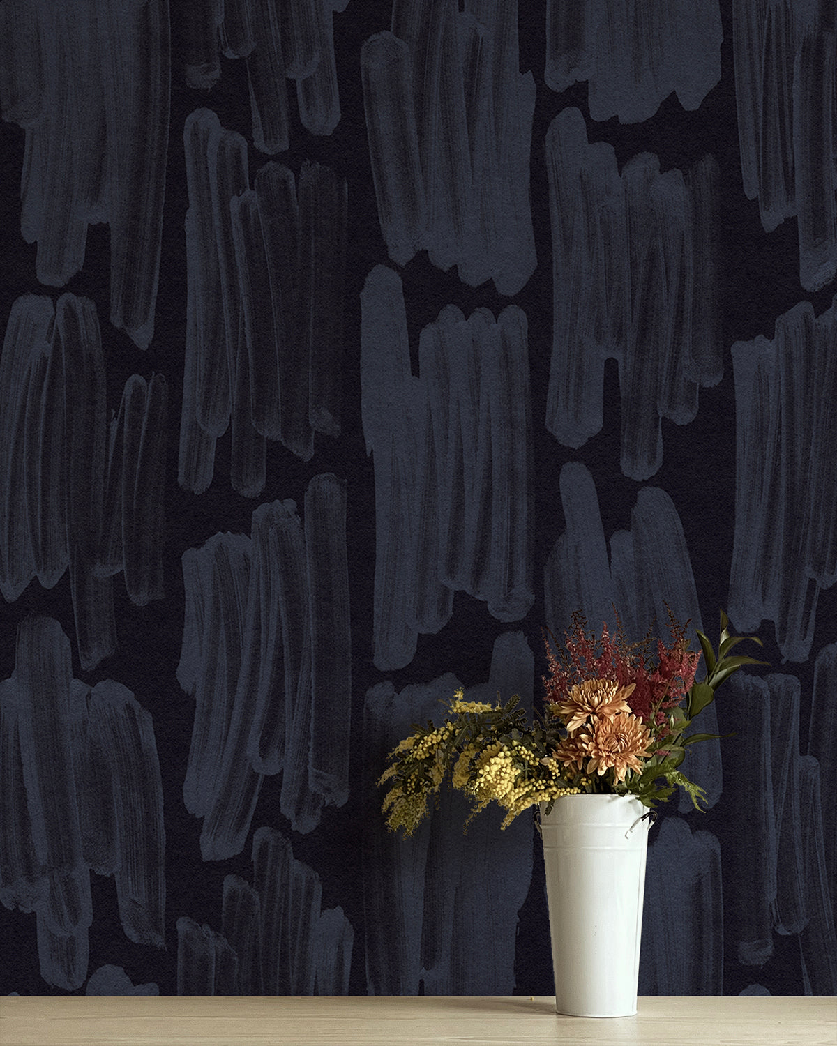 A vase of flowers stands in front of a wall papered in an abstract paint swatch print in blue on a black field.