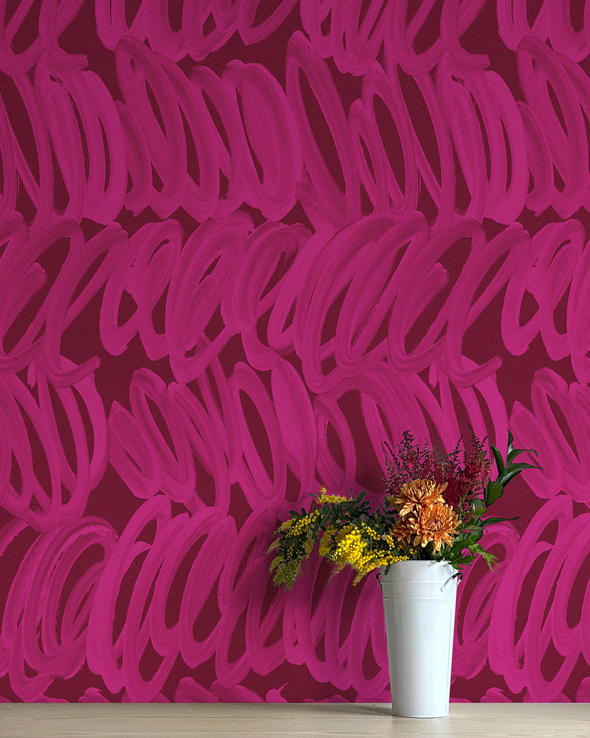 A vase of flowers stands in front of a wall papered in a playful paint print in pink on a maroon field.