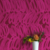 A vase of flowers stands in front of a wall papered in a playful paint print in pink on a maroon field.