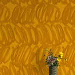 A vase of flowers stands in front of a wall papered in a playful paint print in orange on a yellow field.