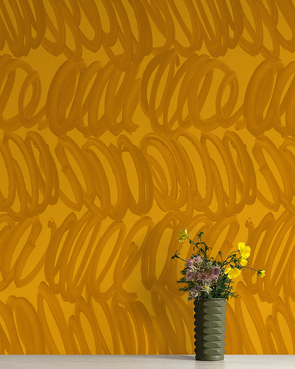 A vase of flowers stands in front of a wall papered in a playful paint print in orange on a yellow field.