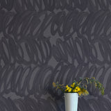 A vase of flowers stands in front of a wall papered in a playful paint print in charcoal on a gray field.