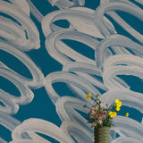 A vase of flowers stands in front of a wall covered in an abstract paintstroke print in cream on a navy field.