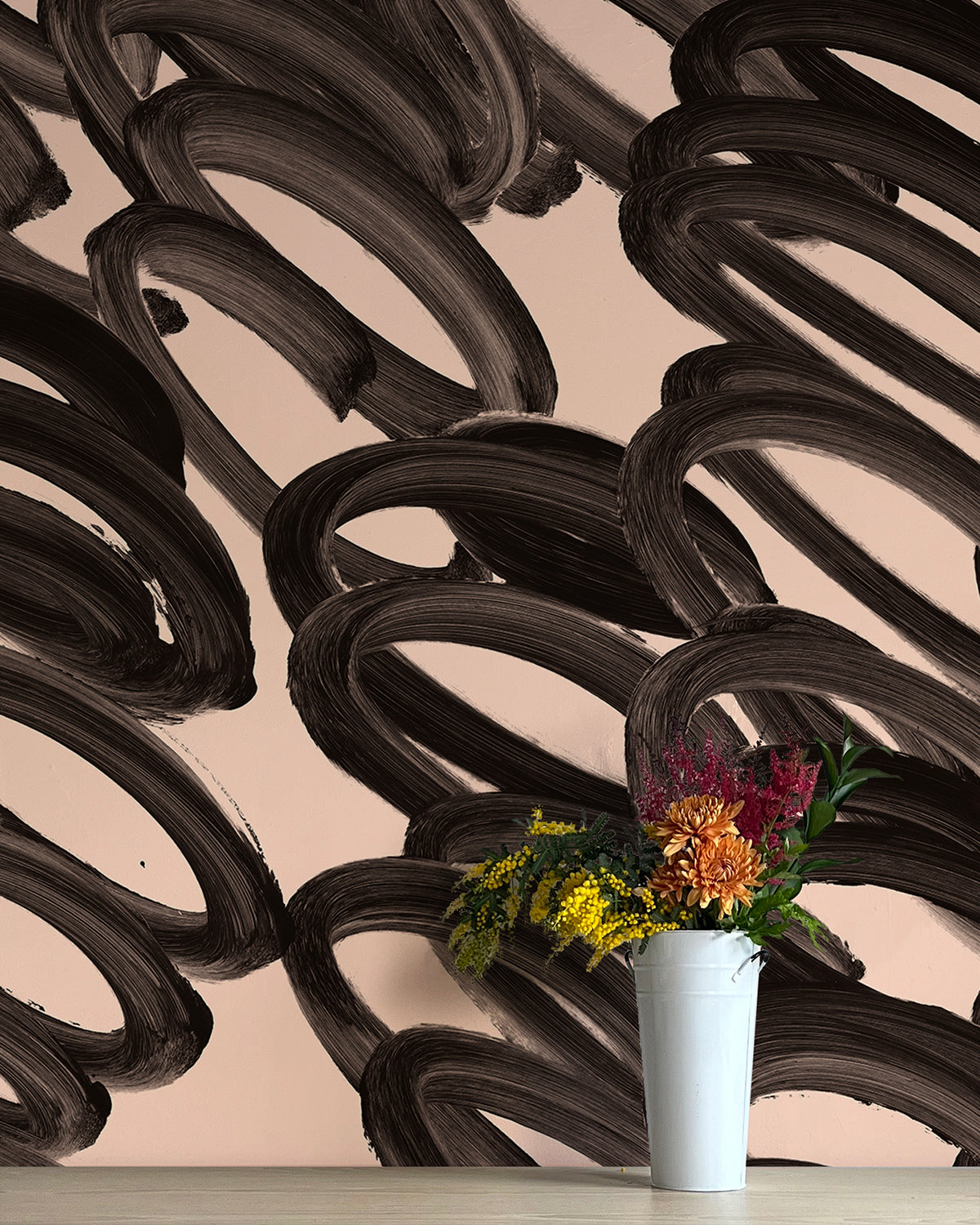 A vase of flowers stands in front of a wall covered in an abstract paintstroke print in black on a cream field.