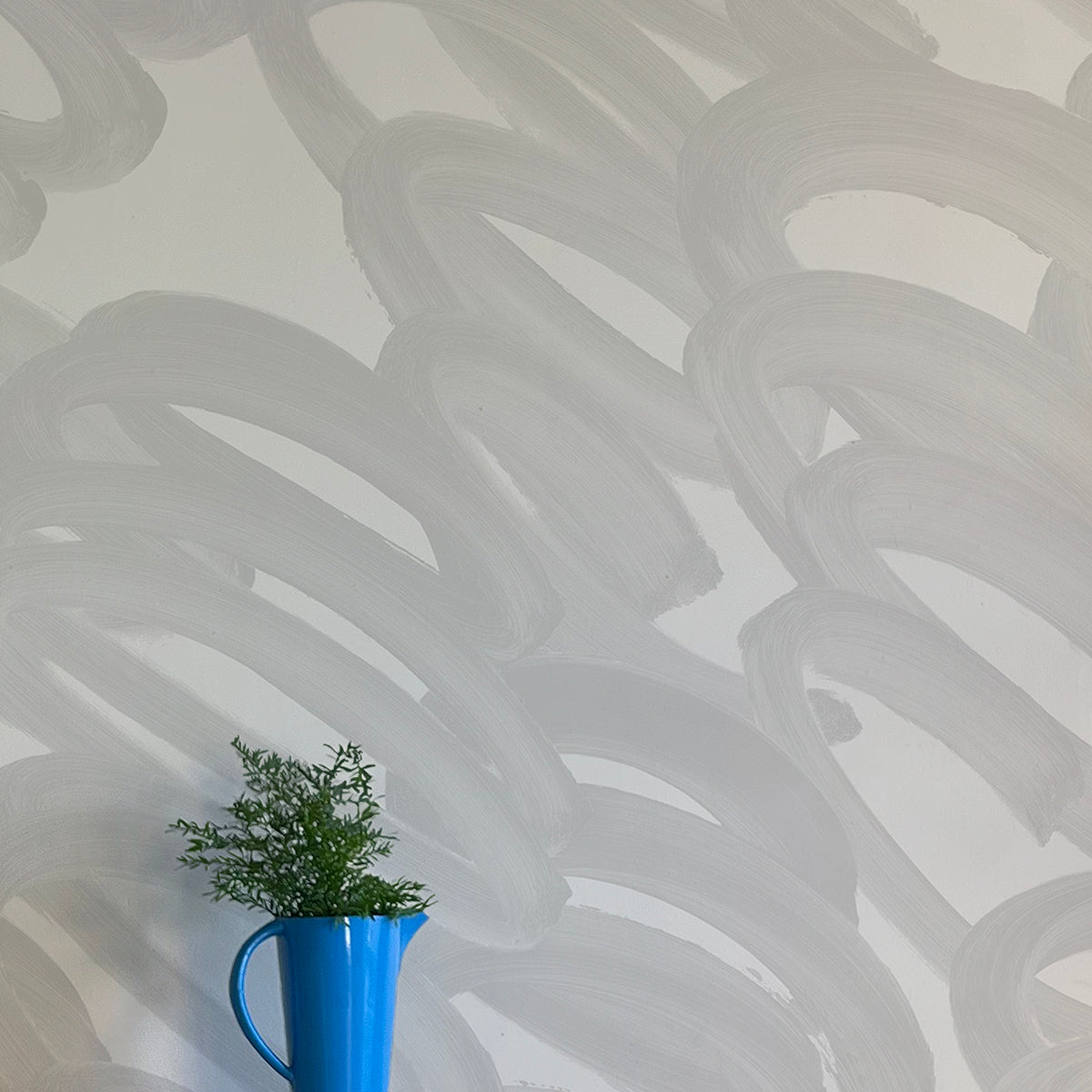 A vase of flowers stands in front of a wall covered in an abstract paintstroke print in gray on a light gray field.