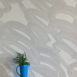 A vase of flowers stands in front of a wall covered in an abstract paintstroke print in gray on a light gray field.