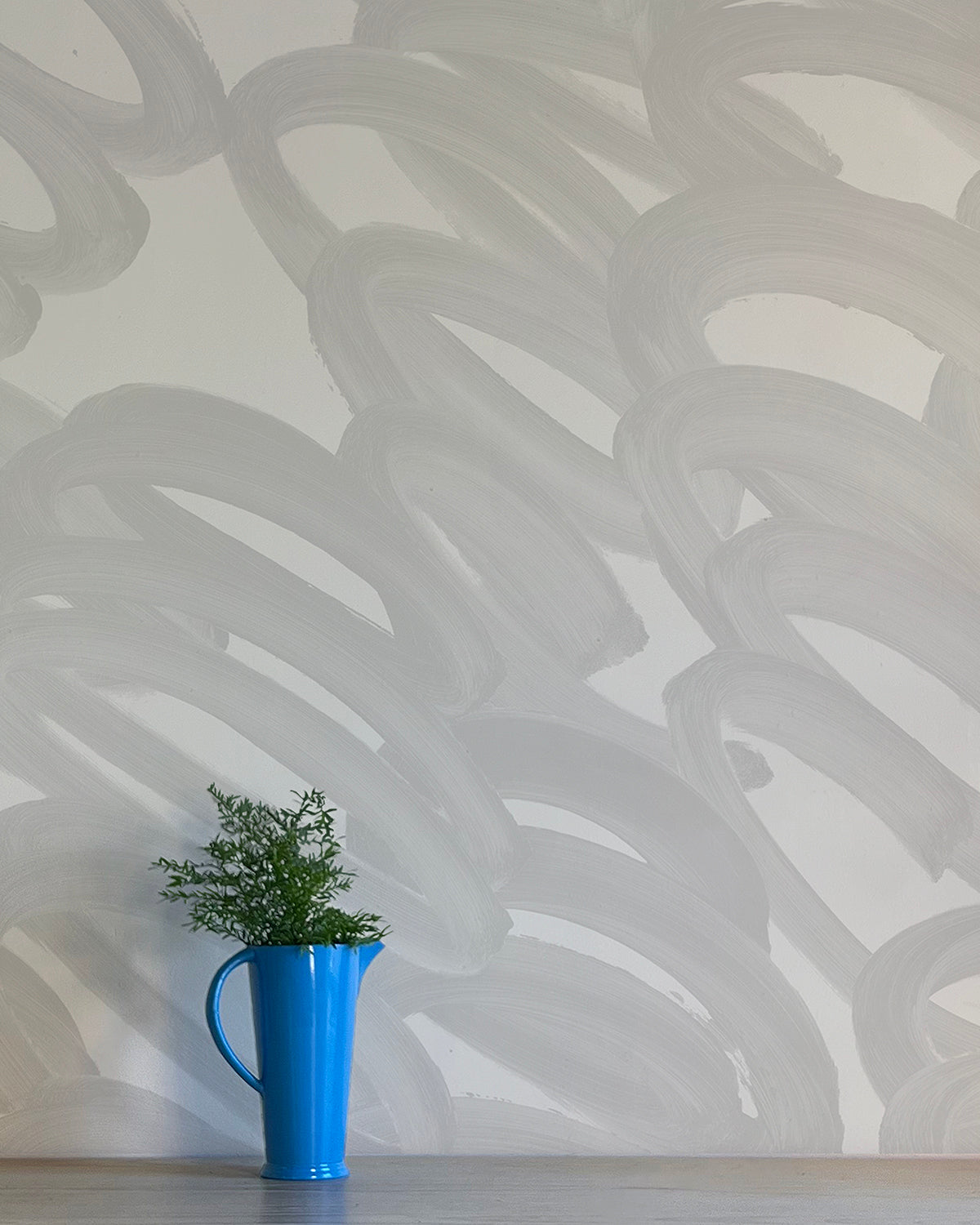 A vase of flowers stands in front of a wall covered in an abstract paintstroke print in gray on a light gray field.