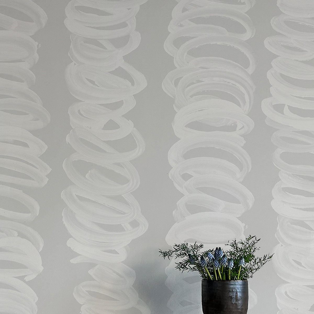 A vase of flowers stands in front of a wall covered in an abstract scribble print in light gray on a gray field.