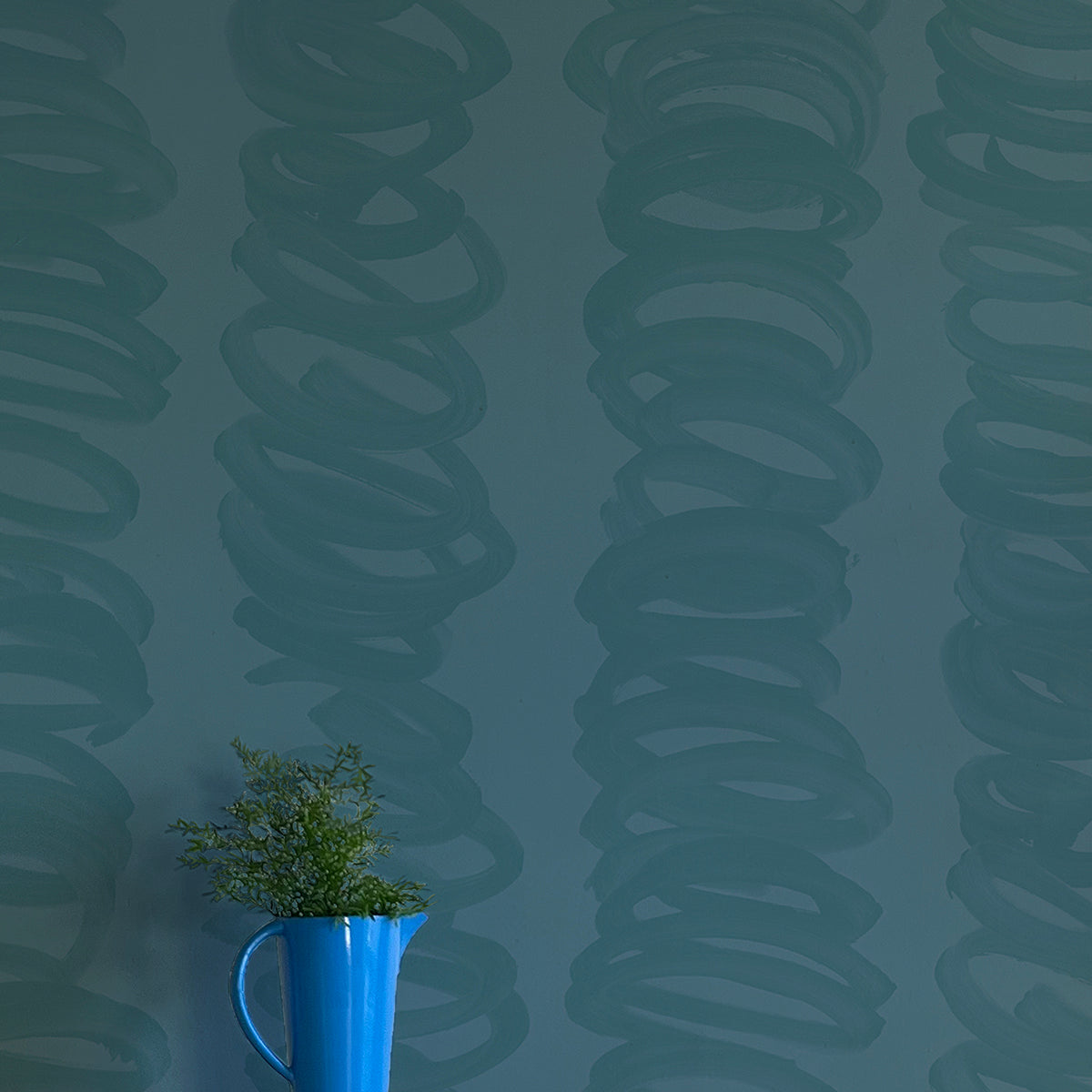 A vase of flowers stands in front of a wall covered in an abstract scribble print in navy on a turquoise field.