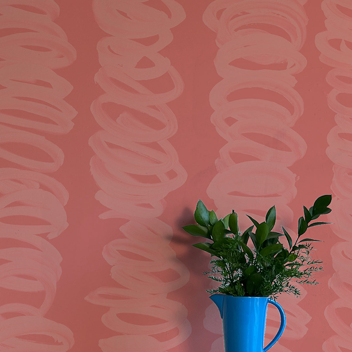 A vase of flowers stands in front of a wall covered in an abstract scribble print in pink on a dark pink field.