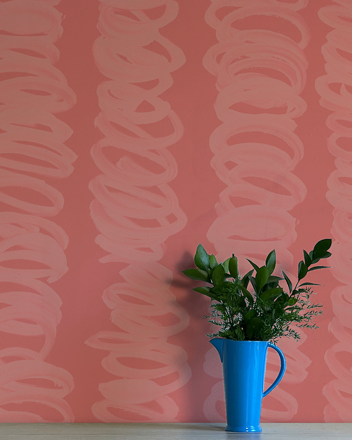 A vase of flowers stands in front of a wall covered in an abstract scribble print in pink on a dark pink field.