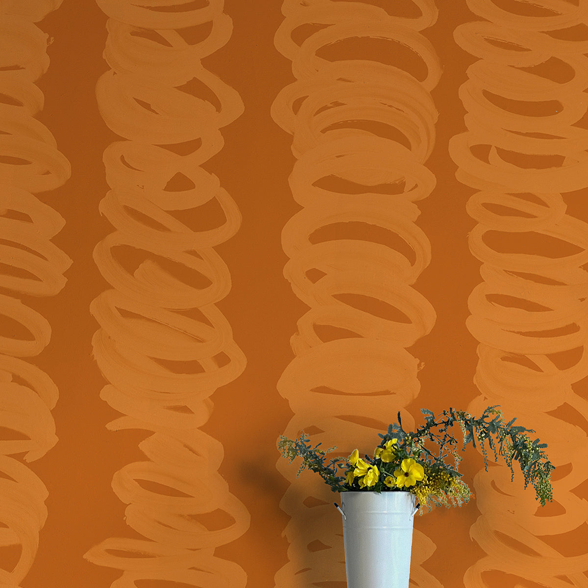 A vase of flowers stands in front of a wall covered in an abstract scribble print in orange on a rust field.