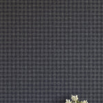 A vase of flowers stands in front of a wall papered in a dense plaid pattern in shades of navy.