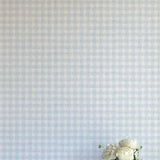 A vase of flowers stands in front of a wall papered in a dense plaid pattern in shades of light blue and cream.